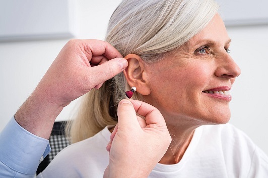 Seniorin bekommt ein modernes Hörgerät eingesetzt, Hörakustiker Beratung und Anpassung.